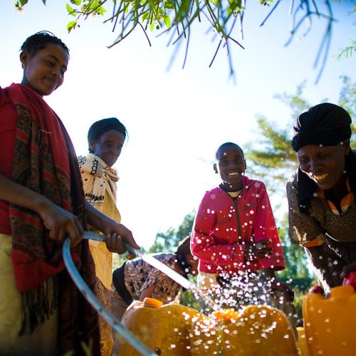 Women and children filling containers from a hose at a water point
